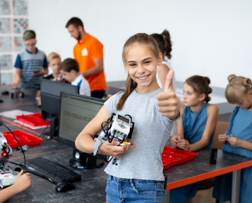 Portrait of a happy schoolgirl girl in a robotics class, she holds a robot assembled from plastic parts programmed on a computer